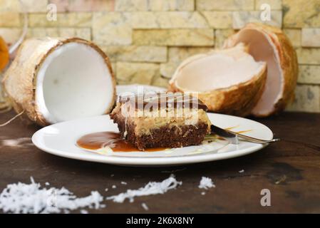 Kokoskuchen auf weißem Teller mit einem Löffel und Karamellsoße Stockfoto