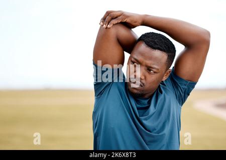 Dehnung ist entscheidend für optimale Funktion und Leistung. Ein sportlicher junger Mann, der seine Arme beim Training im Freien streckt. Stockfoto