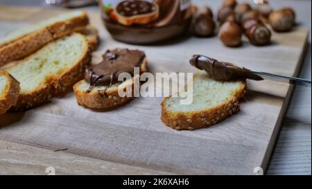 Ein Messer trägt Schokolade und Haselnusscreme auf eine Scheibe frisch gebackenem Brot aus nächster Nähe auf. Erhöhen Sie das hausgemachte Frühstück Stockfoto