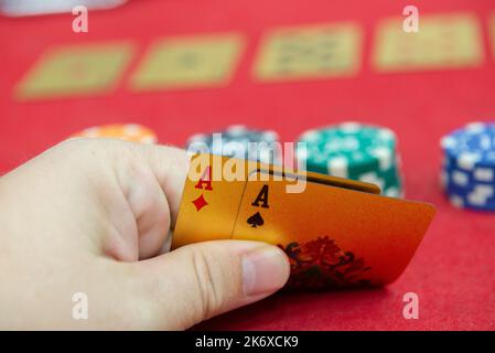 Spielkarten in der Hand auf dem roten Tuch. Eine gewinnende Kombination in Poker Texas Holdem. Zwei Asse und großer Einsatz auf rotem Filz. Zwei Asse auf dem Pokertisch und Stockfoto