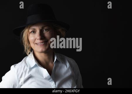 Dezem Porträt einer lächelnden Frau im mittleren Alter, die einen schwarzen Hut trägt. Stockfoto
