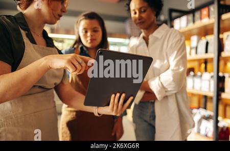 Die Lebensmittelmanagerin verwendet ein digitales Tablet, während sie in einem Mitarbeitergespräch mit ihren Mitarbeitern ein Gespräch führt. Eine Gruppe verschiedener Frauen, die zusammenarbeiten Stockfoto
