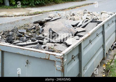 Großer, überladener Abfallcontainer, gefüllt mit Teilen von entferntem Asphalt, Bauabfall in der Nähe einer Baustelle für Straßengraben. Stockfoto