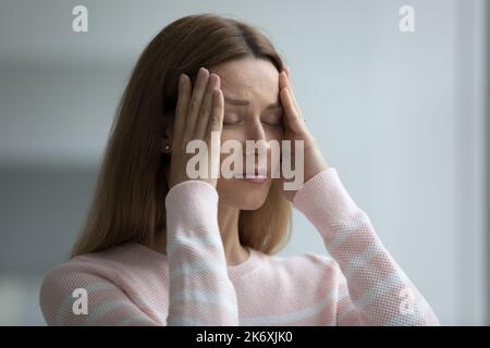 Frau leidet unter starken Kopfschmerzen, Berührungsbügel versuchen, Schmerzen zu lindern Stockfoto