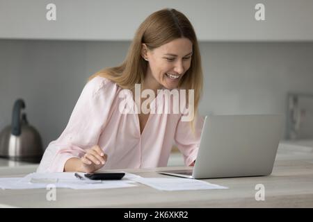 Lächelnde Frau berechnet Einkommen, Kosten auf Rechner Rechnungen online bezahlen Stockfoto