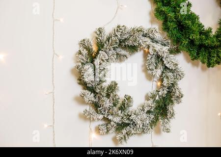An der Wand hängt ein Neujahrskranz aus den Zweigen eines Weihnachtsbaums. Dekorationen im Haus für das neue Jahr. Dekorieren des Raumes für das Neue Stockfoto
