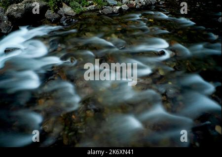 Die Langzeitfotografie verwischt die plätschernde Oberfläche von Andorras Valira del Nord, einem schnell fließenden Fluss, der hoch in den östlichen Pyrenäen aufsteigt und schließlich in die Gran Valira, den größten Wasserlauf des Fürstentums, mündet. Blick auf das Flussbett neben der Pont d’Ordino oder der Pont de l’Estarell, eine Buckelbrücke aus dem 15.. Jahrhundert, die 1980 nördlich von Llorts im Tal von Ordino umgebaut wurde. Stockfoto