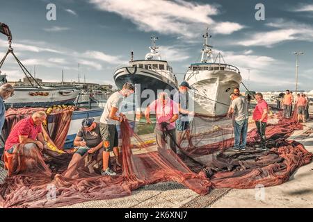 Einheimische Fischer, die ihre Netze im Hafen von Trapani auf Sizilien ausbessern Stockfoto