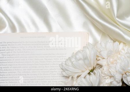 Schönes Blumenkonzept, weiße Chrysantheme auf den Büchern über weißem Stoffhintergrund. Stockfoto