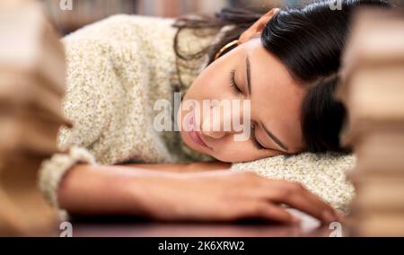 Ich mache nur ein kurzes Nickerchen. Eine junge Frau schläft, während sie in einer Bibliothek am College studiert. Stockfoto