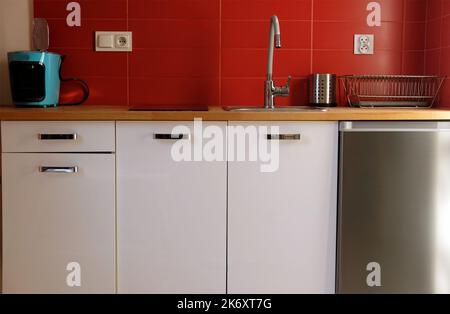 Reihe von modernen weißen Küchenschränken mit roten Fliesen Wand, Holz Arbeitsplatte und Edelstahl-Geräte Kühlschrank in einem kleinen Apartment Stockfoto