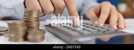 Eine Frau zählt auf einen grauen Rechner neben den Münzen, Stockfoto