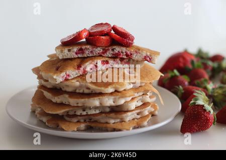 Erdbeerpfannkuchen. Weiche und flauschige Buttermilchpfannkuchen mit frischen Erdbeeren, die mit frisch geschnittenen Erdbeeren zubereitet werden, dem Teig aus Mehl hinzugefügt, b Stockfoto