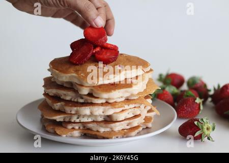 Erdbeerpfannkuchen. Weiche und flauschige Buttermilchpfannkuchen mit frischen Erdbeeren, die mit frisch geschnittenen Erdbeeren zubereitet werden, dem Teig aus Mehl hinzugefügt, b Stockfoto