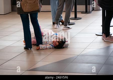 Lima, Peru - 27 2022. Juli: Ein kleines Mädchen, das auf dem Boden im Wartezimmer in der Mitte des Boarding-Bereichs am Flughafen liegt Stockfoto