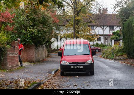 Postbote mit rotem königlichen Briefwagen, der im Herbst Briefe in Micheldever Village, Hampshire, England, Großbritannien, auslieferte Stockfoto