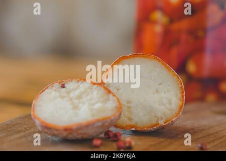 Eine Nahaufnahme der belper-Kugeln mit Knoblauch und rosa Pfeffer in Holzasche. Schweizer Käse. Milchig fermentierter Käse. Und Jalapeno auf dem Hintergrund konserviert. SDOF Stockfoto