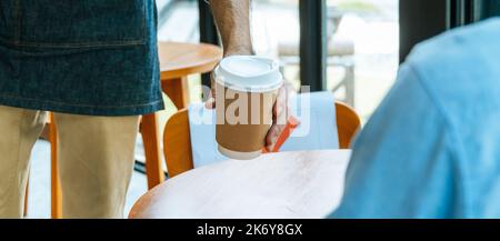 Das Personal mit einer Schürze und einer verkürzten Aussicht servierte dem Gast auf dem Tisch im Café-Café, im Café-Restaurant, im Inhaber eines kleinen Unternehmens und im Service eine heiße schwarze Kaffeetasse Stockfoto