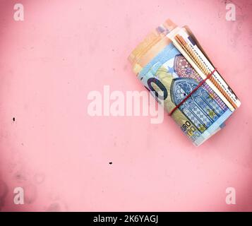 Rolle von 20-Euro-Banknoten (innen 50 und 100 Euro) mit rotem Gummiband. Geld/Finanzen auf rosa Hintergrund Stockfoto