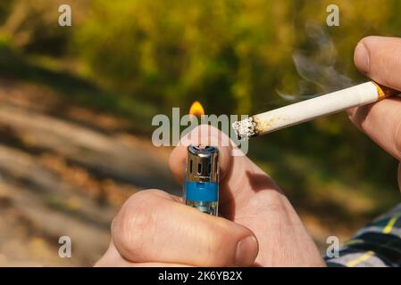 Die Hand zündet eine Zigarette mit einem Feuerzeug an. Rauchen schadet der Gesundheit einer Person. Zigaretten Stockfoto