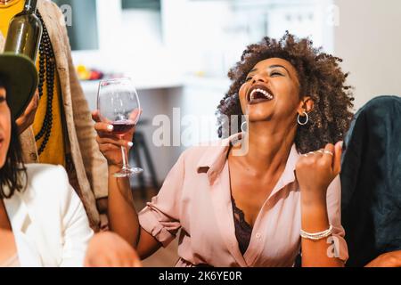 Portrait einer afroamerikanischen Frau, die lachend Wein trinkt, mit ihren Freunden beim Essen auf einer multiethnischen Party sitzt - People Lifestyle-Konzept Stockfoto
