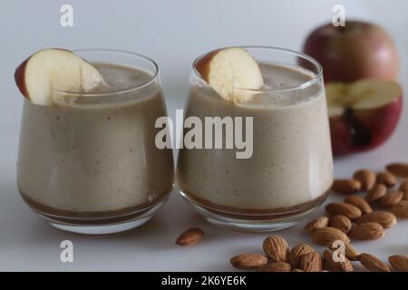 Apfelmilch schütteln. Sommergetränk Milchshake aus Mandelmilch und gefrorenen Äpfeln. Aufgenommen auf weißem Hintergrund mit Apfel und Mandeln. Stockfoto