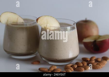 Apfelmilch schütteln. Sommergetränk Milchshake aus Mandelmilch und gefrorenen Äpfeln. Aufgenommen auf weißem Hintergrund mit Apfel und Mandeln. Stockfoto