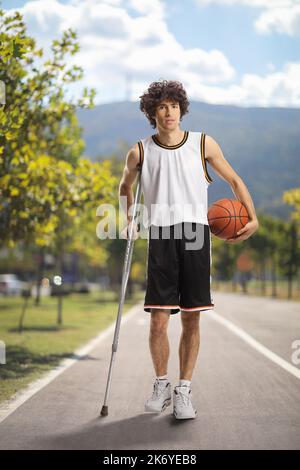 Basketballspieler hält einen Ball und läuft mit einer Krücke auf einem Fußgängerweg Stockfoto