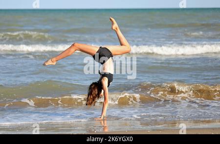 Junges barfuss Mädchen in schwarzem Badeanzug von rhythmischen Gymnastikübungen am Meer Stockfoto