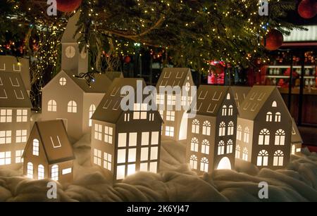 Kleine Spielzeug-Weihnachtshäuser mit brennendem Licht vor dem Hintergrund des Weihnachtsbaums Stockfoto