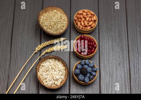 Zutaten für ein ausgewogenes Frühstück. Haferflocken, Preiselbeeren und Heidelbeeren in Holzschüsseln. Weizenkörner und Weizenkörner in einer Schüssel. Speicherplatz kopieren. Fla Stockfoto