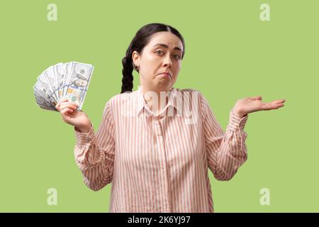 Investitionen. Eine zweifelnd junge, hübsche kaukasische Frau hält einen Fan von Dollars und breitet ihre Arme auf die Seiten aus. Isoliert auf hellgrünem Hintergrund. Th Stockfoto