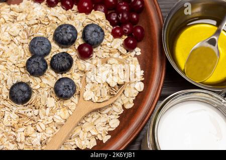 Ungekochte Haferflocken mit Beeren. Joghurt im Glas, Honig in Metallschüssel. Teil des Rahmens. Nahaufnahme. Stockfoto