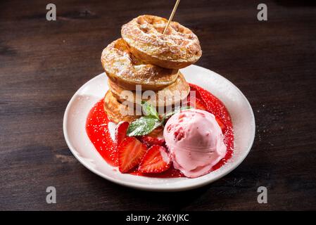 Runde geschwollene Waffeln mit Erdbeereis, bestreut mit Puderzucker und beträufelt mit Erdbeersirup. Stockfoto