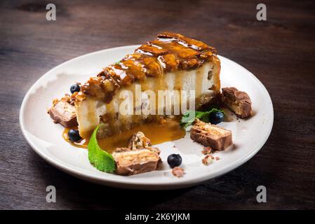 Käsekuchen mit Karamellgeschmack. Eine Scheibe Dessert mit gesalzenem Karamellsirup, Erdnüssen und Milchschokolade. Der Käsekuchen wird mit Blauer garniert Stockfoto