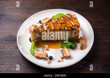 Käsekuchen mit Karamellgeschmack. Eine Scheibe Dessert mit gesalzenem Karamellsirup, Erdnüssen und Milchschokolade. Der Käsekuchen wird mit Blauer garniert Stockfoto