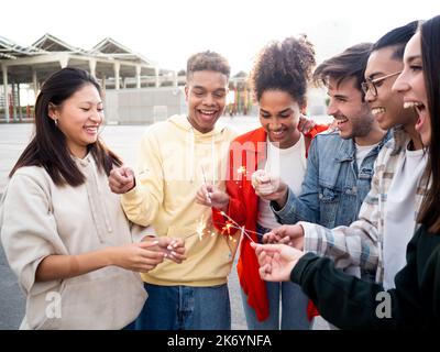 Gruppe von verschiedenen Millennial jungen Freunden, die Spaß mit Wunderkerzen haben. Union, Vielfalt, beste Freunde Stockfoto