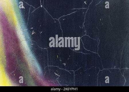 Alte schwarz gestrichene rissige Wand mit verschmierten farbigen Flecken Stockfoto