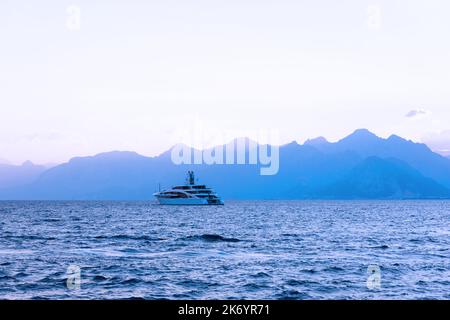 yacht segelt das Meer bei Sonnenuntergang vor der Kulisse der Berge Stockfoto