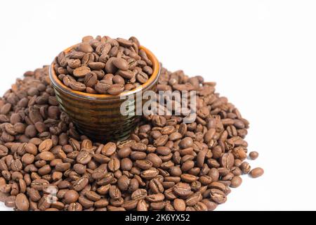 Eine kleine Untertasse mit Kaffeebohnen steht auf einem Haufen Kaffee auf weißem Hintergrund, Platz kopieren und Platz für Text. Stockfoto