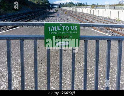 Ein Schild in der Nähe einer Eisenbahnlinie in Dublin, Irland, für die Samariter, auf dem unruhige Menschen aufgefordert werden, mit den Samaritanern zu sprechen, Stockfoto