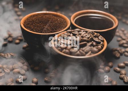 Tassen Kaffee zwischen ausgewählten und kalibrierten Arabica-Kaffeebohnen, die auf schwarzem Hintergrund verstreut sind. Stockfoto