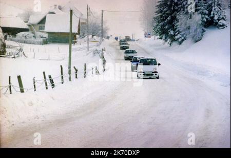 Fahrzeugreihe auf einer verschneiten Straße im Kreis Brasov, Rumänien, ca. 1999. Stockfoto