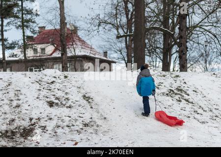 Ein Junge mit einem roten Schlitten auf einer Rutsche. Stockfoto