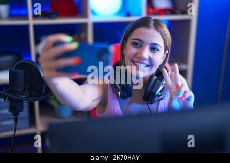 Junge schöne hispanische Frau streamer lächelnd zuversichtlich machen Selfie per Smartphone im Spielzimmer Stockfoto