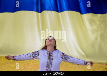 Sie betet für die Ukraine eine junge Frau hält die Flagge der Ukraine in ihren Händen, während sie ihren Kopf in den Himmel hebt. Stockfoto