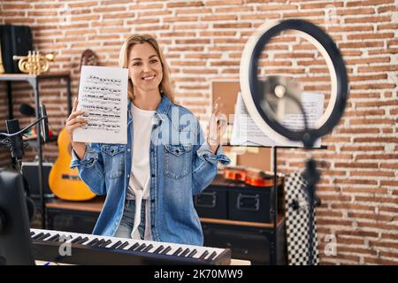 Junge kaukasische Frau macht Online-Musik-Tutorial zeigt Noten lächelnd glücklich zeigen mit Hand und Finger zur Seite Stockfoto