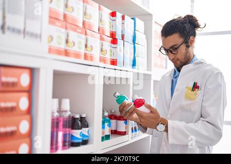 Junger hispanic-Mann Apotheker hält Medikamentenflaschen in der Apotheke Stockfoto