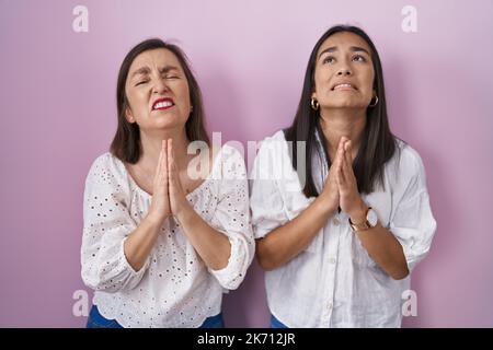 Hispanische Mutter und Tochter betteln und beten zusammen mit den Händen und dem Ausdruck der Hoffnung im Gesicht sehr emotional und besorgt. Betteln. Stockfoto