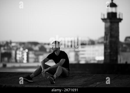 Ein hübscher junger Mann sitzt auf der Promenade. Schwarzweiß-Foto. Stockfoto